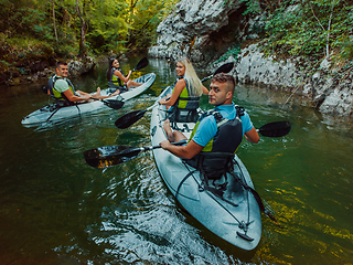 Image showing A group of friends enjoying having fun and kayaking while exploring the calm river, surrounding forest and large natural river canyons