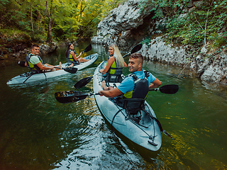 Image showing A group of friends enjoying having fun and kayaking while exploring the calm river, surrounding forest and large natural river canyons