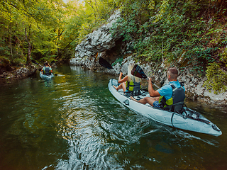 Image showing A group of friends enjoying having fun and kayaking while exploring the calm river, surrounding forest and large natural river canyons