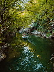 Image showing A group of friends enjoying having fun and kayaking while exploring the calm river, surrounding forest and large natural river canyons