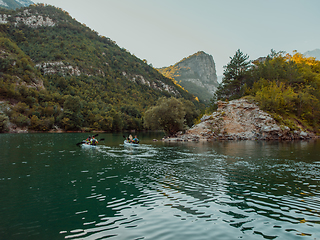 Image showing A group of friends enjoying having fun and kayaking while exploring the calm river, surrounding forest and large natural river canyons