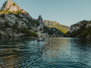 Image showing A group of friends enjoying having fun and kayaking while exploring the calm river, surrounding forest and large natural river canyons