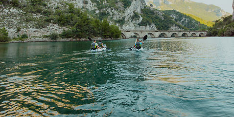 Image showing A group of friends enjoying having fun and kayaking while exploring the calm river, surrounding forest and large natural river canyons