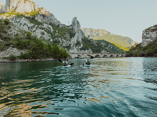 Image showing A group of friends enjoying having fun and kayaking while exploring the calm river, surrounding forest and large natural river canyons