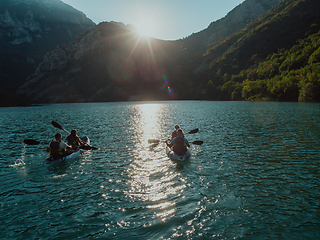 Image showing A group of friends enjoying fun and kayaking exploring the calm river, surrounding forest and large natural river canyons during an idyllic sunset.