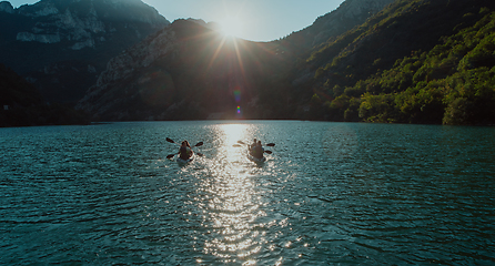 Image showing A group of friends enjoying fun and kayaking exploring the calm river, surrounding forest and large natural river canyons during an idyllic sunset.