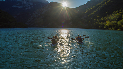 Image showing A group of friends enjoying fun and kayaking exploring the calm river, surrounding forest and large natural river canyons during an idyllic sunset.