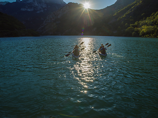 Image showing A group of friends enjoying fun and kayaking exploring the calm river, surrounding forest and large natural river canyons during an idyllic sunset.