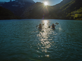 Image showing A group of friends enjoying fun and kayaking exploring the calm river, surrounding forest and large natural river canyons during an idyllic sunset.