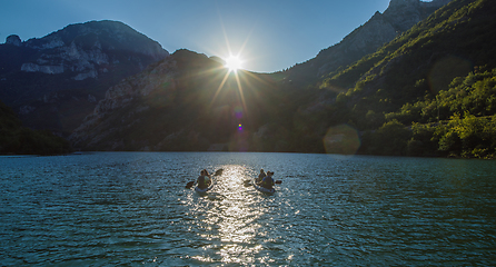 Image showing A group of friends enjoying fun and kayaking exploring the calm river, surrounding forest and large natural river canyons during an idyllic sunset.