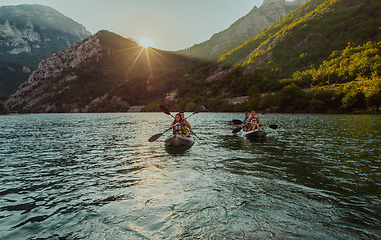 Image showing A group of friends enjoying fun and kayaking exploring the calm river, surrounding forest and large natural river canyons during an idyllic sunset.