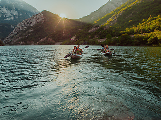 Image showing A group of friends enjoying fun and kayaking exploring the calm river, surrounding forest and large natural river canyons during an idyllic sunset.