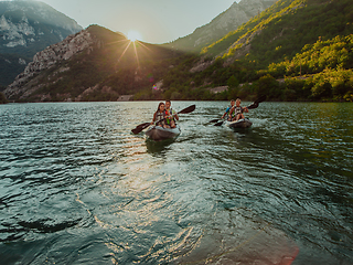 Image showing A group of friends enjoying fun and kayaking exploring the calm river, surrounding forest and large natural river canyons during an idyllic sunset.