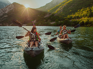 Image showing A group of friends enjoying fun and kayaking exploring the calm river, surrounding forest and large natural river canyons during an idyllic sunset.