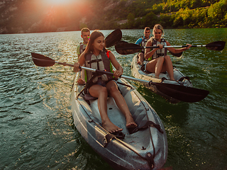 Image showing A group of friends enjoying fun and kayaking exploring the calm river, surrounding forest and large natural river canyons during an idyllic sunset.