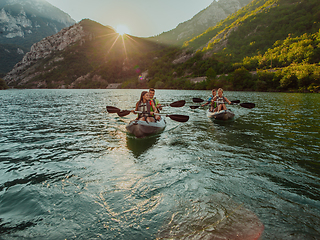 Image showing A group of friends enjoying fun and kayaking exploring the calm river, surrounding forest and large natural river canyons during an idyllic sunset.