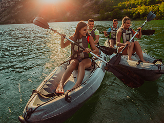 Image showing A group of friends enjoying fun and kayaking exploring the calm river, surrounding forest and large natural river canyons during an idyllic sunset.