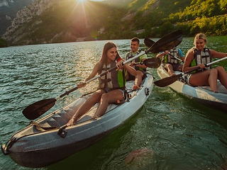 Image showing A group of friends enjoying fun and kayaking exploring the calm river, surrounding forest and large natural river canyons during an idyllic sunset.