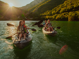 Image showing A group of friends enjoying fun and kayaking exploring the calm river, surrounding forest and large natural river canyons during an idyllic sunset.