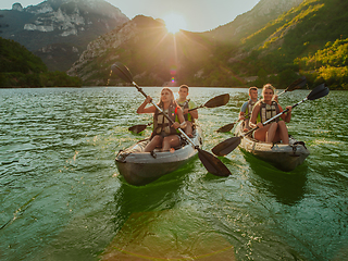 Image showing A group of friends enjoying fun and kayaking exploring the calm river, surrounding forest and large natural river canyons during an idyllic sunset.