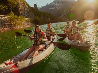 Image showing A group of friends enjoying fun and kayaking exploring the calm river, surrounding forest and large natural river canyons during an idyllic sunset.