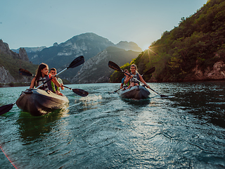 Image showing A group of friends enjoying fun and kayaking exploring the calm river, surrounding forest and large natural river canyons during an idyllic sunset.