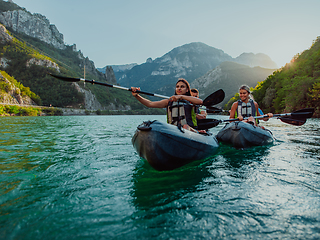 Image showing A group of friends enjoying fun and kayaking exploring the calm river, surrounding forest and large natural river canyons during an idyllic sunset.