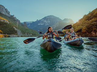 Image showing A group of friends enjoying fun and kayaking exploring the calm river, surrounding forest and large natural river canyons during an idyllic sunset.