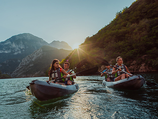 Image showing A group of friends enjoying fun and kayaking exploring the calm river, surrounding forest and large natural river canyons during an idyllic sunset.