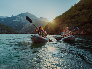 Image showing A group of friends enjoying fun and kayaking exploring the calm river, surrounding forest and large natural river canyons during an idyllic sunset.