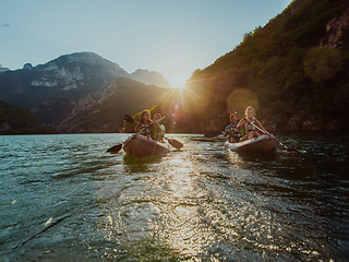 Image showing A group of friends enjoying fun and kayaking exploring the calm river, surrounding forest and large natural river canyons during an idyllic sunset.