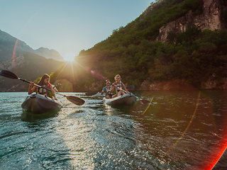 Image showing A group of friends enjoying fun and kayaking exploring the calm river, surrounding forest and large natural river canyons during an idyllic sunset.