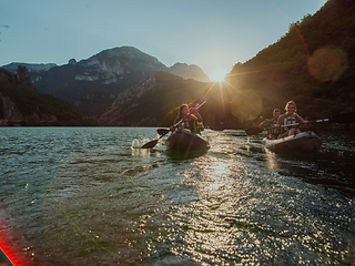 Image showing A group of friends enjoying fun and kayaking exploring the calm river, surrounding forest and large natural river canyons during an idyllic sunset.