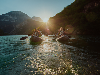 Image showing A group of friends enjoying fun and kayaking exploring the calm river, surrounding forest and large natural river canyons during an idyllic sunset.