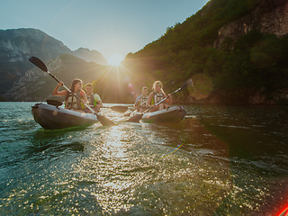 Image showing A group of friends enjoying fun and kayaking exploring the calm river, surrounding forest and large natural river canyons during an idyllic sunset.