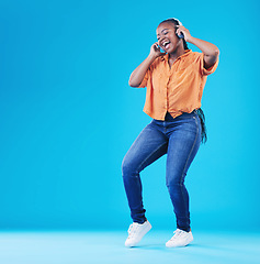 Image showing Black woman, headphones and dancing to music with singing in a studio. Audio streaming, radio and happy female person with blue background and excited from celebration and freedom with hip hop song