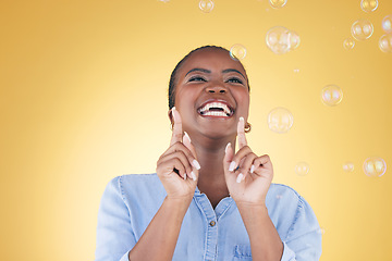 Image showing Excited, happy and black woman on yellow background with bubbles for happiness, joy and fun. Playful laugh, smile and isolated African person in studio with soap bubble for freedom, magic and color