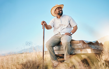 Image showing Happy, African farmer and land in the countryside and man, sitting and watching over agriculture, field and environment. Farming, meadow and worker outdoor with smile in summer with happiness