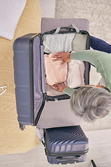 Image showing Top view, travel and woman with clothes in suitcase for adventure, holiday and international vacation. Home, bedroom and above of mature person packing clothing in luggage prepare for trip or journey