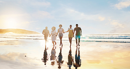 Image showing Friends, together and walking on beach at sunset in water in summer, vacation or holiday break with freedom. Group, silhouette and people with connection, holding hands and support in community