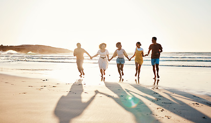 Image showing Friends, holding hands and running at sunset on beach in summer or walking together on holiday in California with freedom. Group, silhouette or vacation with connection or support in community