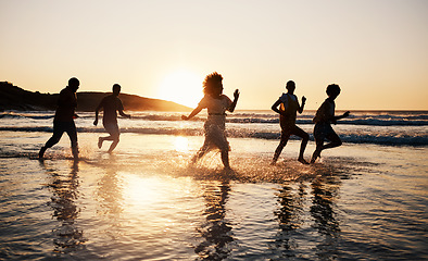Image showing Sunset, beach and friends with freedom, running and having fun in water together on summer vacation. Ocean, silhouette and group of people at the sea for holiday, bond and travel celebration in Bali