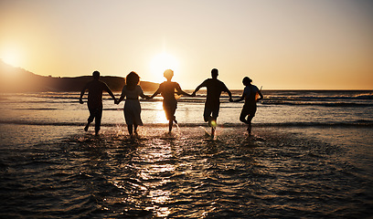 Image showing Water splash, sunset and friends holding hands at a beach with freedom, running or fun vacation rear view. Ocean, silhouette and people shadow in solidarity at the sea for travel, bond or celebration