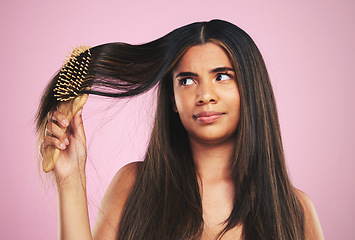 Image showing Woman, hair and worry with brush in studio for texture, shine and keratin on pink background. Natural beauty, face and young model thinking with comb tools for tangled hairstyle, knot and treatment