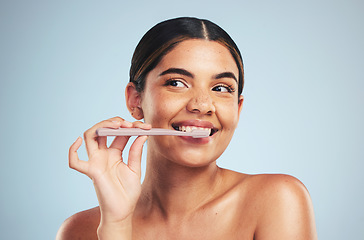 Image showing Woman, happy and brushing teeth in studio for healthy dental wellness on blue background. Face of model thinking with toothbrush while cleaning mouth for fresh breath, oral hygiene or care of smile