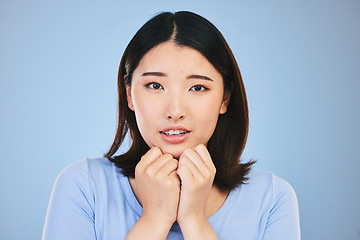 Image showing Asian, portrait and scared woman with surprise from announcement, news or horror story on blue background in studio. Shock, face and person in danger with fear in facial expression, hands or reaction