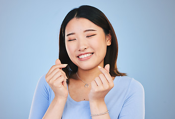 Image showing Happy asian woman, hands and love sign or gesture in romance against a blue studio background. Face of calm female person smile in happiness with loving emoji, icon or symbol for valentines day