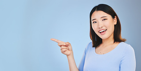 Image showing Asian woman, point and studio portrait with space, mockup and happy for promotion by blue background. Japanese student, girl and smile for review, opinion or feedback with choice, decision and sign