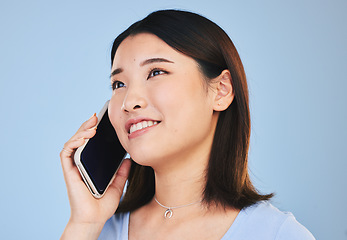 Image showing Asian woman, thinking and phone call in studio with chat, networking and smile by blue background. Young Japanese student, girl and smartphone for contact, mobile connection and memory with ideas