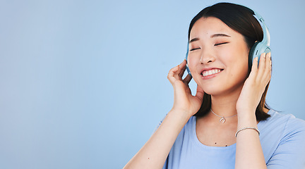 Image showing Face of happy Asian woman in studio with headphones for streaming radio, subscription and relax. Sound, smile and person listen to music, audio and track for calm on mockup space on blue background